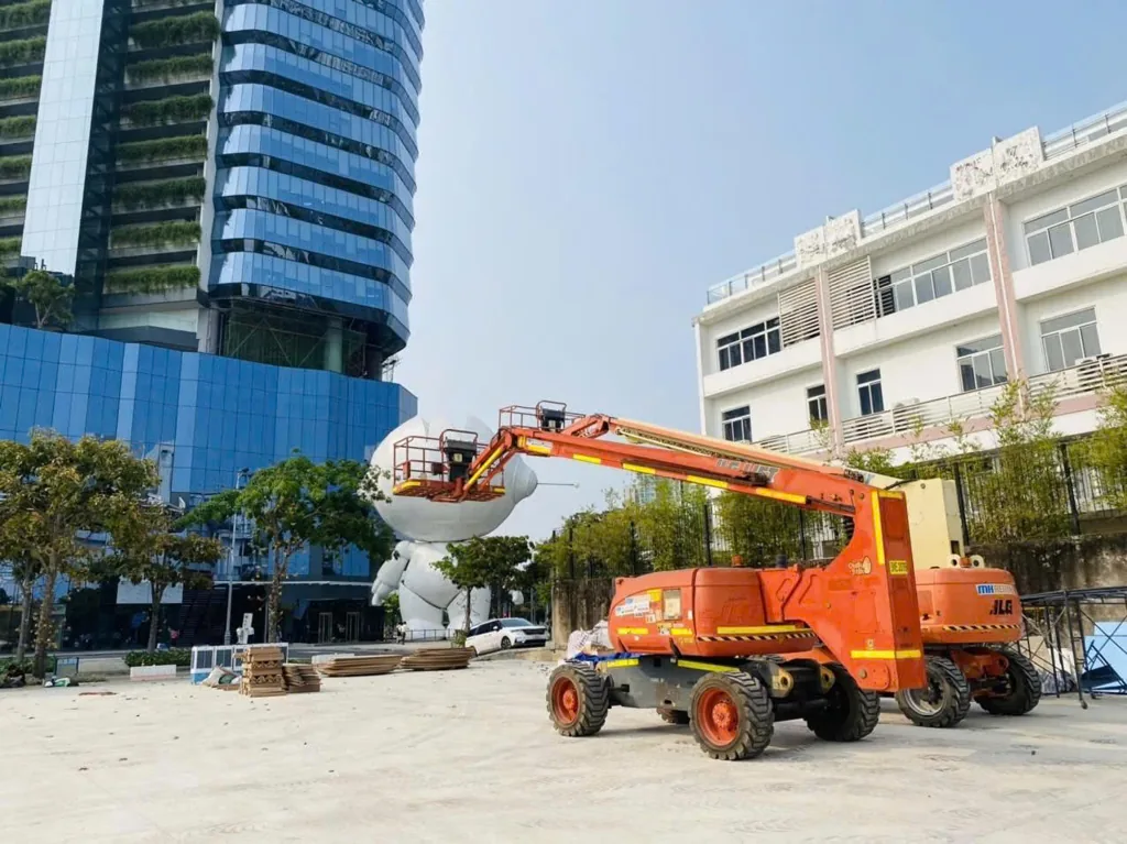 Xe nâng người MH Rental tại Sofic Tower với tòa nhà kính ở hậu cảnh